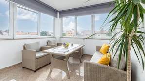 A sunroom with wicker furniture, a glass table, and a view of buildings through large windows. - Awesome apartment in Valbandon with WiFi (Valbandon)