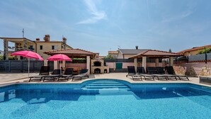 A swimming pool with lounge chairs and umbrellas, surrounded by buildings with tiled roofs. - Awesome apartment in Valbandon with WiFi (Valbandon)