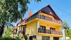 A two-story building with a yellow facade, a red roof, and a balcony with a black railing. - Holiday home with barbecue and garden furniture (Siófok)