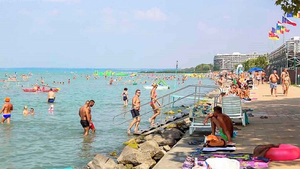 A crowded beach with people swimming and sunbathing, a lifeguard tower, and a pier with umbrellas and beach chairs. - Holiday home with barbecue and garden furniture (Siófok)