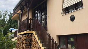 A two-story building with a wooden staircase, a satellite dish, and a stack of firewood outside. - Holiday home with barbecue and garden furniture (Siófok)