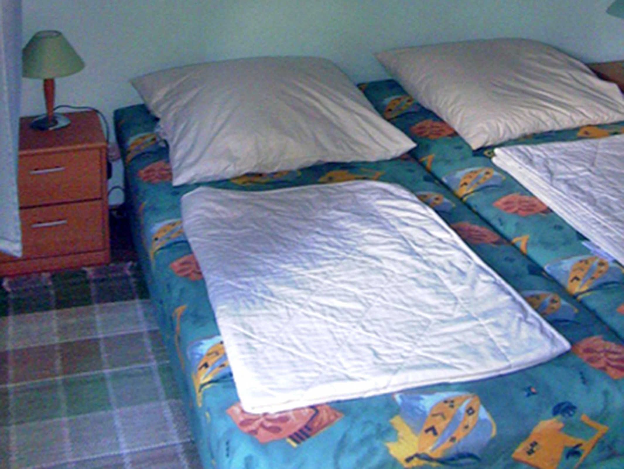 A bedroom with a bed, pillows, a nightstand, and a lamp.