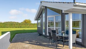Eine moderne Außenpatio mit Tisch und Stühlen, großen Fenstern und Blick auf ein grünes Feld.