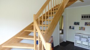 A wooden staircase leading to a landing with a white wall and a small white shelf with folded towels.