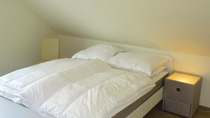 A single bed with white bedding in a room with a sloped ceiling.