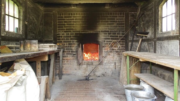 A narrow brick room with a fireplace, wooden benches, and metal buckets.