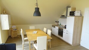 A compact kitchen with a microwave, oven, and dishwasher. There is a dining table with chairs and a hanging light fixture.