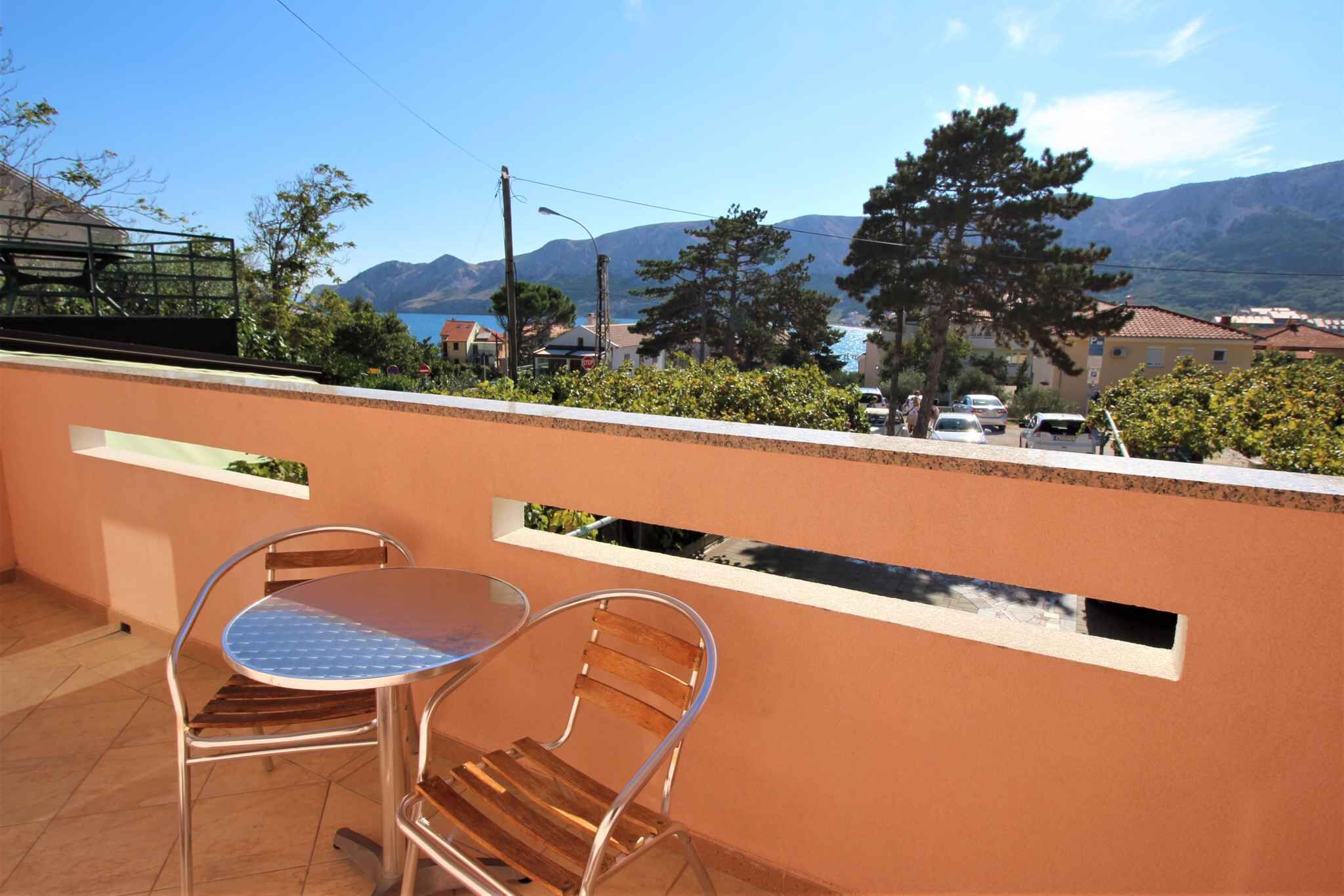 Un balcon avec une table et des chaises, offrant une vue panoramique sur les montagnes et un plan d’eau.