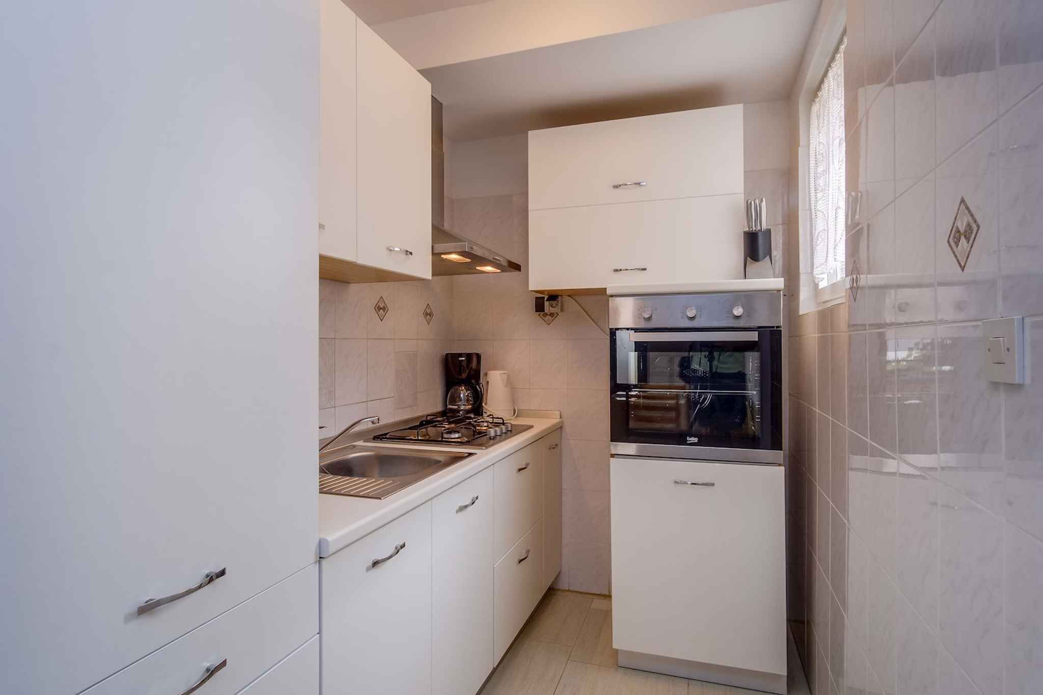 Une cuisine compacte avec des meubles blancs, une cuisinière à gaz, un four encastré et une machine à café.