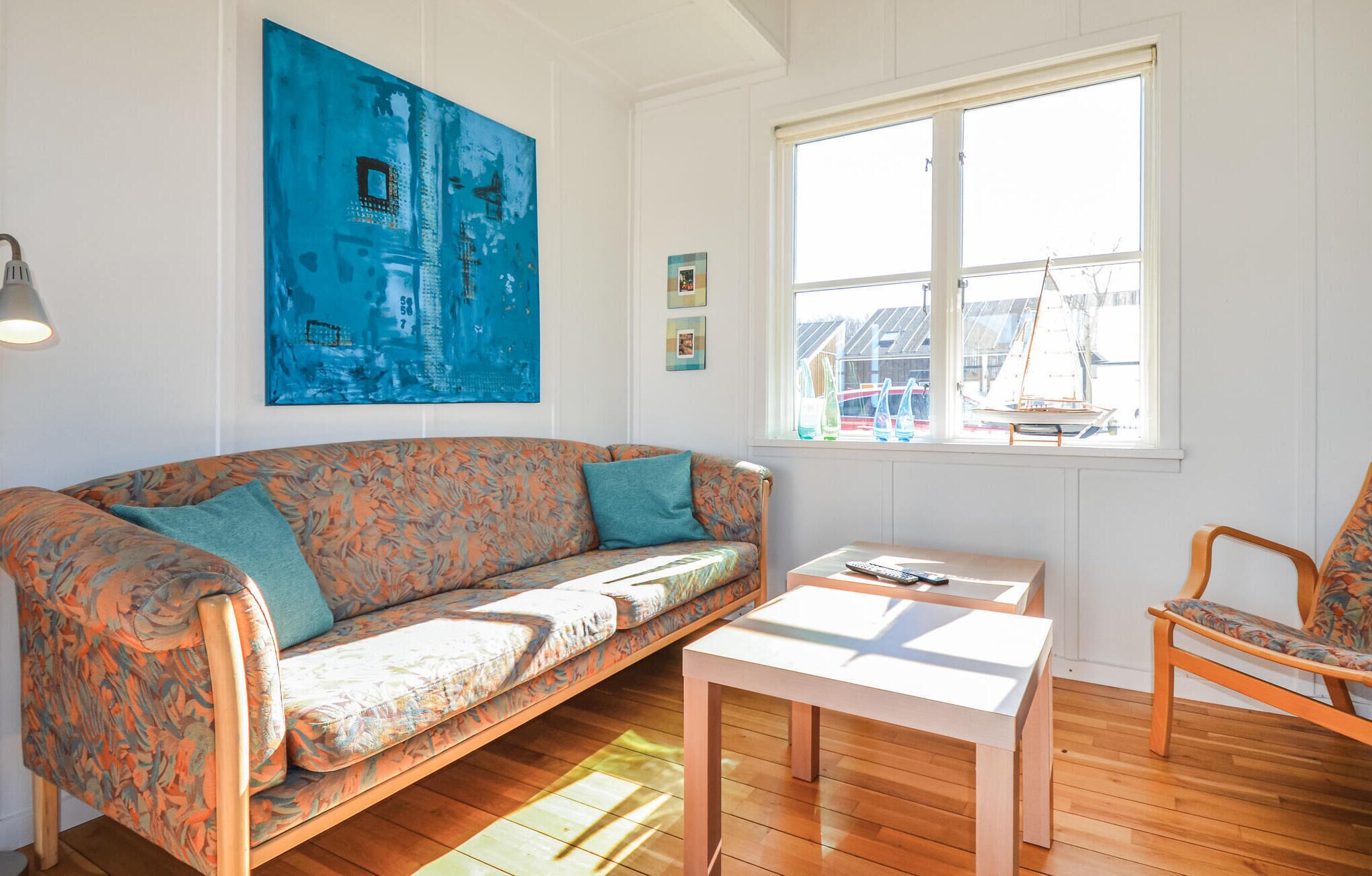 Una habitación acogedora con un sofá floral, una mesita pequeña y un ventanal con vistas a barcos.