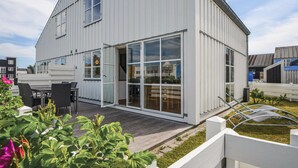 Une maison moderne dotée d’une grande porte vitrée, d’un patio avec des meubles d’extérieur et d’une clôture blanche.