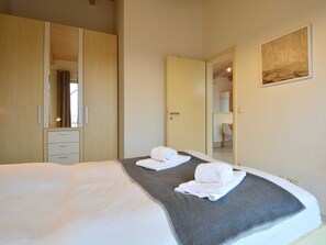 A hotel room with a large bed, a wardrobe, a desk, and a chair.