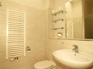 Une salle de bain avec des toilettes blanches, un lavabo, un miroir et un porte-serviettes.