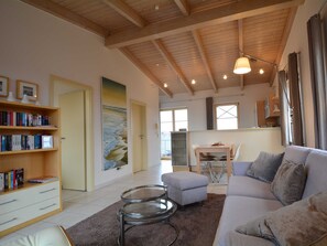 A spacious living area with a high ceiling, a sofa, a coffee table, a bookshelf, and a painting of a beach scene.