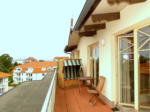 A balcony with a wooden table and chairs, a wicker chair, and a striped awning.