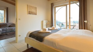 A bedroom with a large bed, a view of the outdoors, a balcony, and a sofa in the adjacent room. - Residence Seestern Whg S-13. - See-13 (Kühlungsborn)