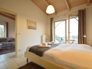 Une chambre avec un grand lit, une vue sur l’extérieur, un balcon et un canapé dans la pièce adjacente.
