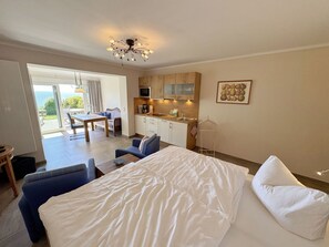 A bedroom with a large bed, a sofa, a dining table, and a kitchen area.