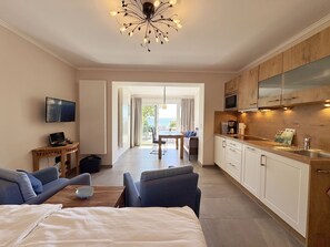 A modern hotel room with a kitchenette, a dining area, and a large bed.