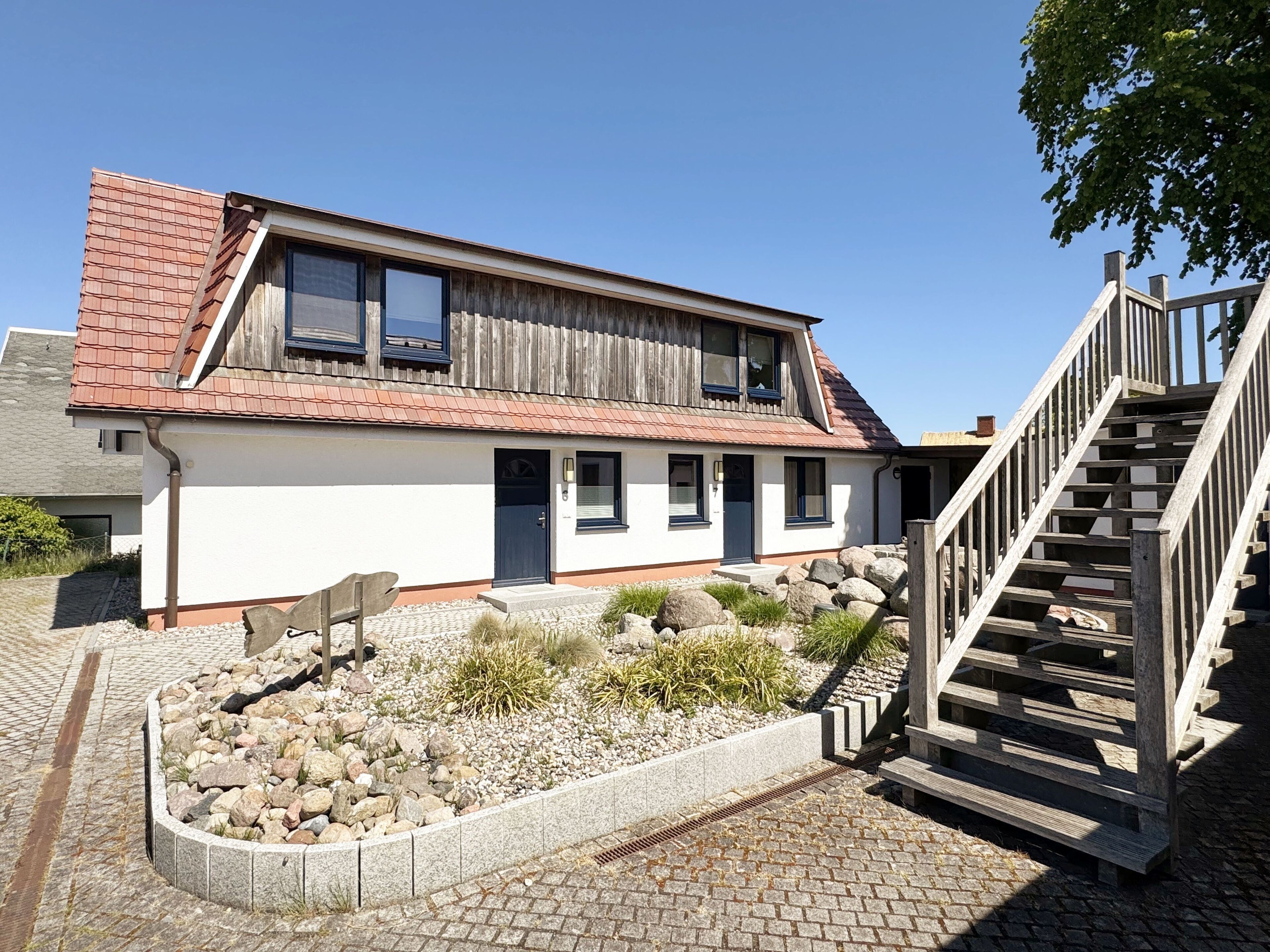 Une maison à deux étages, dotée d’un toit en pente, d’un porche à l’avant et d’un escalier en bois menant à l’étage supérieur.