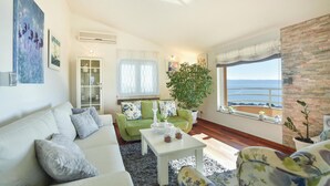 A living room with a white sofa, green armchair, and a large window with a view of the sea. - Stunning home in Podstrana with sauna (Podstrana)