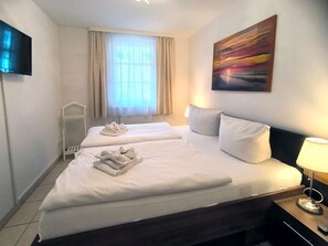 Une chambre d’hôtel avec deux lits, une télévision, un tableau et une fenêtre avec des rideaux.