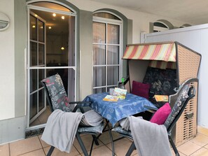 Un comedor con una mesa lista para dos, sillas, una mesita con mantel azul y una ventana con cortinas.