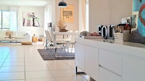 A modern living room with a white sofa, dining table, and chairs. There is a large window with curtains, a painting on the wall, and a decorative vase on the coffee table. - Awesome home in St Nazaire de Ladarez (St Nazaire de Ladarez)