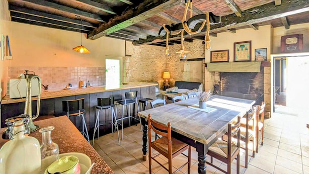 A rustic kitchen with a wooden table and chairs, a hanging light fixture, and a stone wall. - 2 bedroom stunning home in Grignols (Grignols)