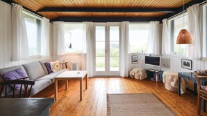 Une pièce chaleureuse avec un plafond en bois, un canapé, une table, un téléviseur et une fenêtre avec des rideaux.
