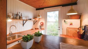 Une cuisine avec des meubles de rangement en bois, un évier, deux plantes en pot et une fenêtre donnant sur un paysage verdoyant.