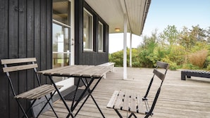 Une terrasse en bois avec une table et deux chaises, un porche couvert et une vue sur la verdure.