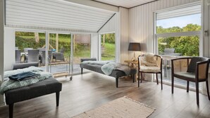 Ein großzügiger Wohnbereich mit Sofa, Sesseln und Couchtisch. Große Fenster bieten Ausblick ins Freie.