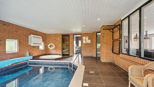 Ein moderner Innenpool mit Backsteinwand, Whirlpool und Korbstuhl.