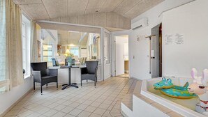 A hotel room with a tiled floor, a dining area with wicker chairs, a small table with a vase of flowers, and a children's play area with inflatable toys. - Amazing home in Oksbøl with sauna (Oksbøl)