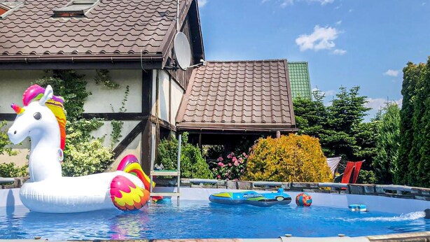 Ein Swimmingpool mit aufblasbaren Spielzeugen, einem weißen Einhorn-Schwimmtier und einem Haus mit Ziegeldach im Hintergrund.
