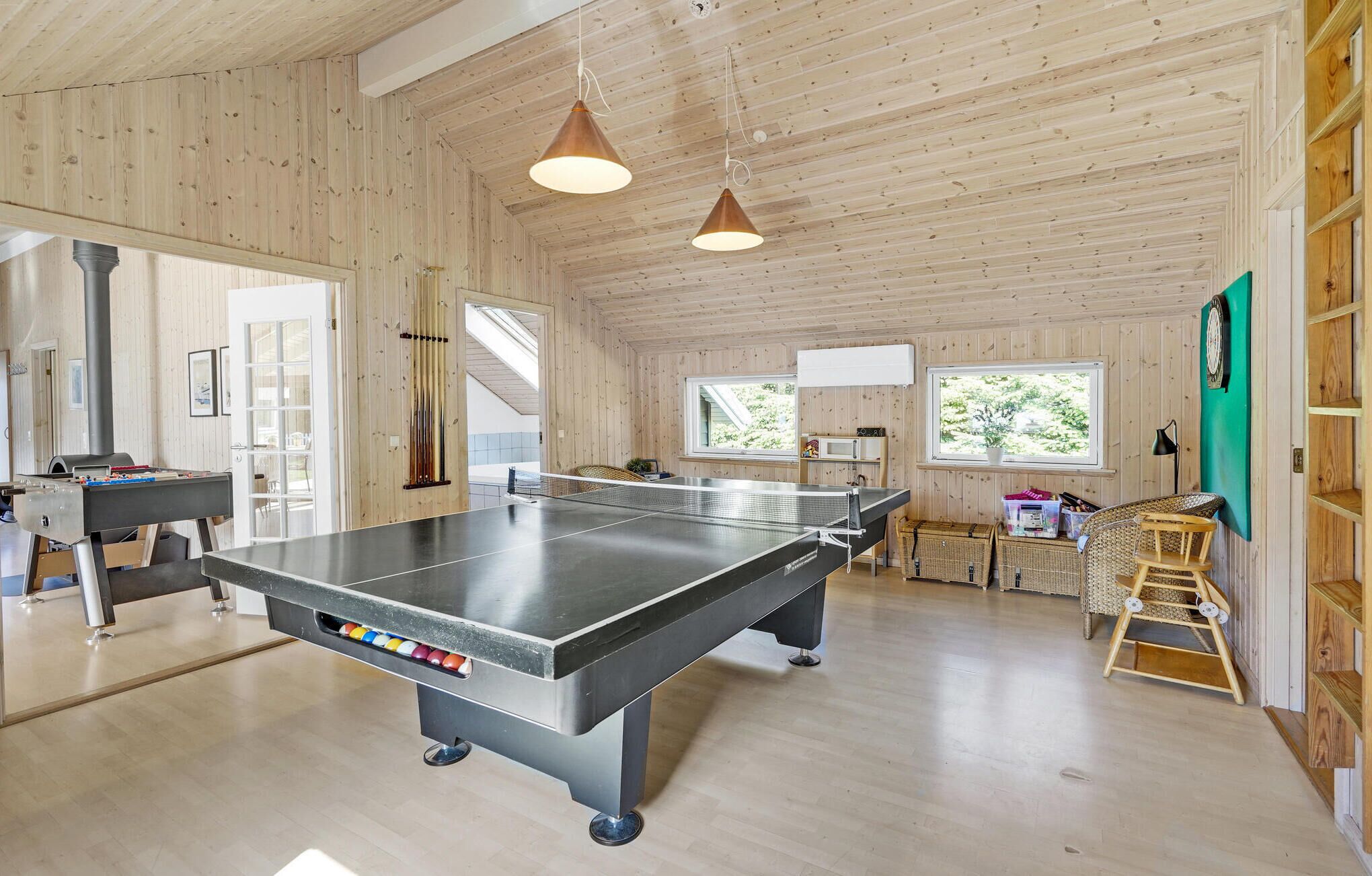 A spacious indoor area with a ping pong table, wooden walls, and a ping pong table with a ball rack.