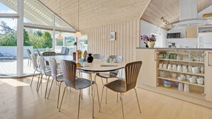 A modern kitchen with a dining area, featuring wooden paneling, a large window, and a variety of kitchen appliances. - Beautiful home in Væggerløse with sauna (Væggerløse)