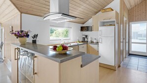 A modern kitchen with a central island, wooden cabinets, a built-in microwave, and a refrigerator. - Beautiful home in Væggerløse with sauna (Væggerløse)