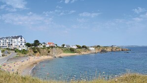 Eine Küstenlandschaft mit Strand, einem großen Gebäude mit mehreren Balkonen und blauem Himmel.