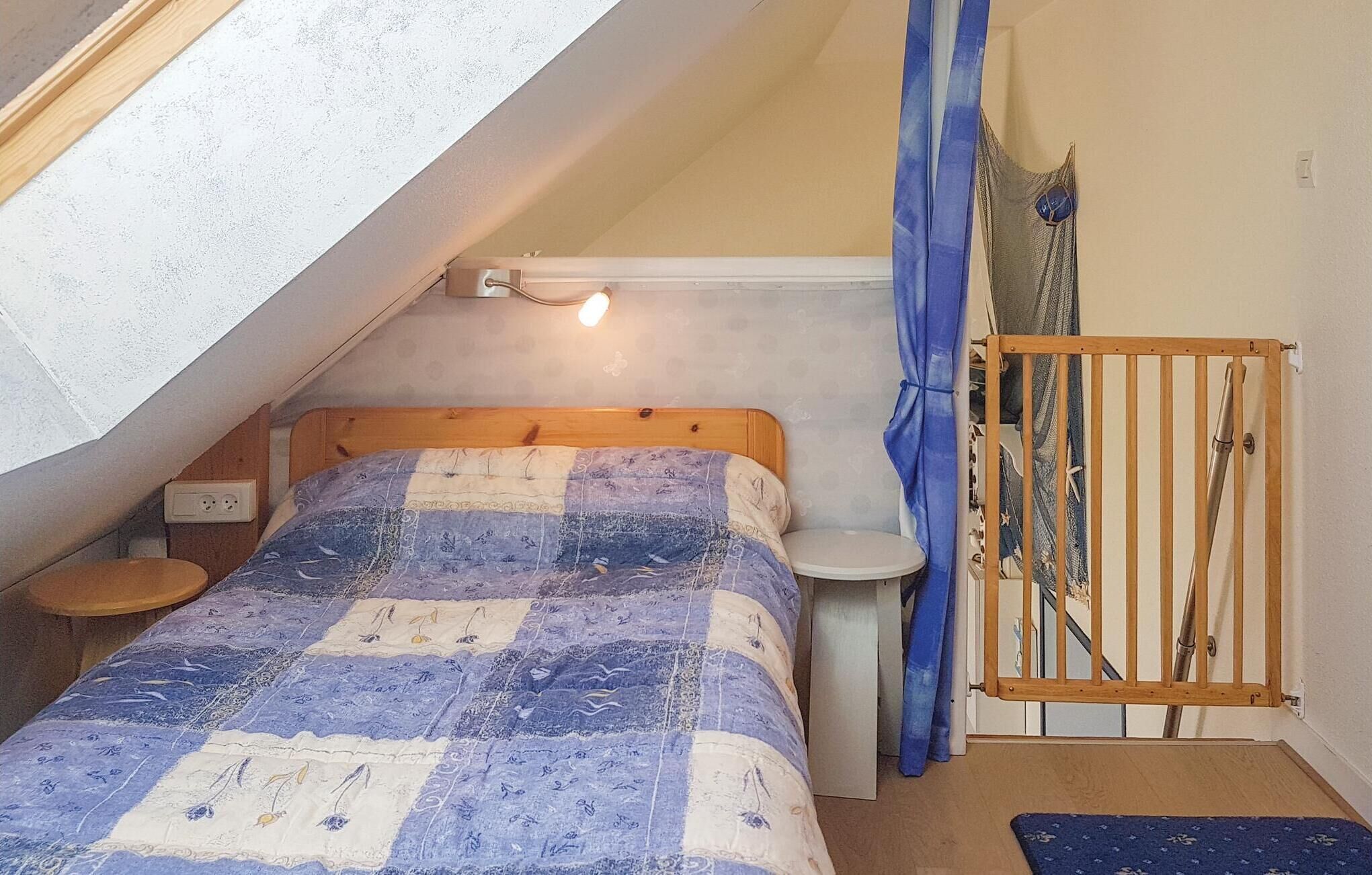 A small, cozy room with a sloped ceiling, a wooden bed, a bedside table, a small stool, and a curtain.
