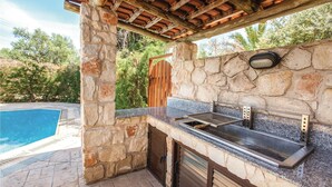 Une cuisine extérieure avec un mur en pierre, une piscine et une pergola en bois.