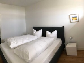 A double bed with white bedding, a black headboard, a small bedside table with a lamp, and a framed picture on the wall. - Apartment 10 - gate to the sea (Helgoland)