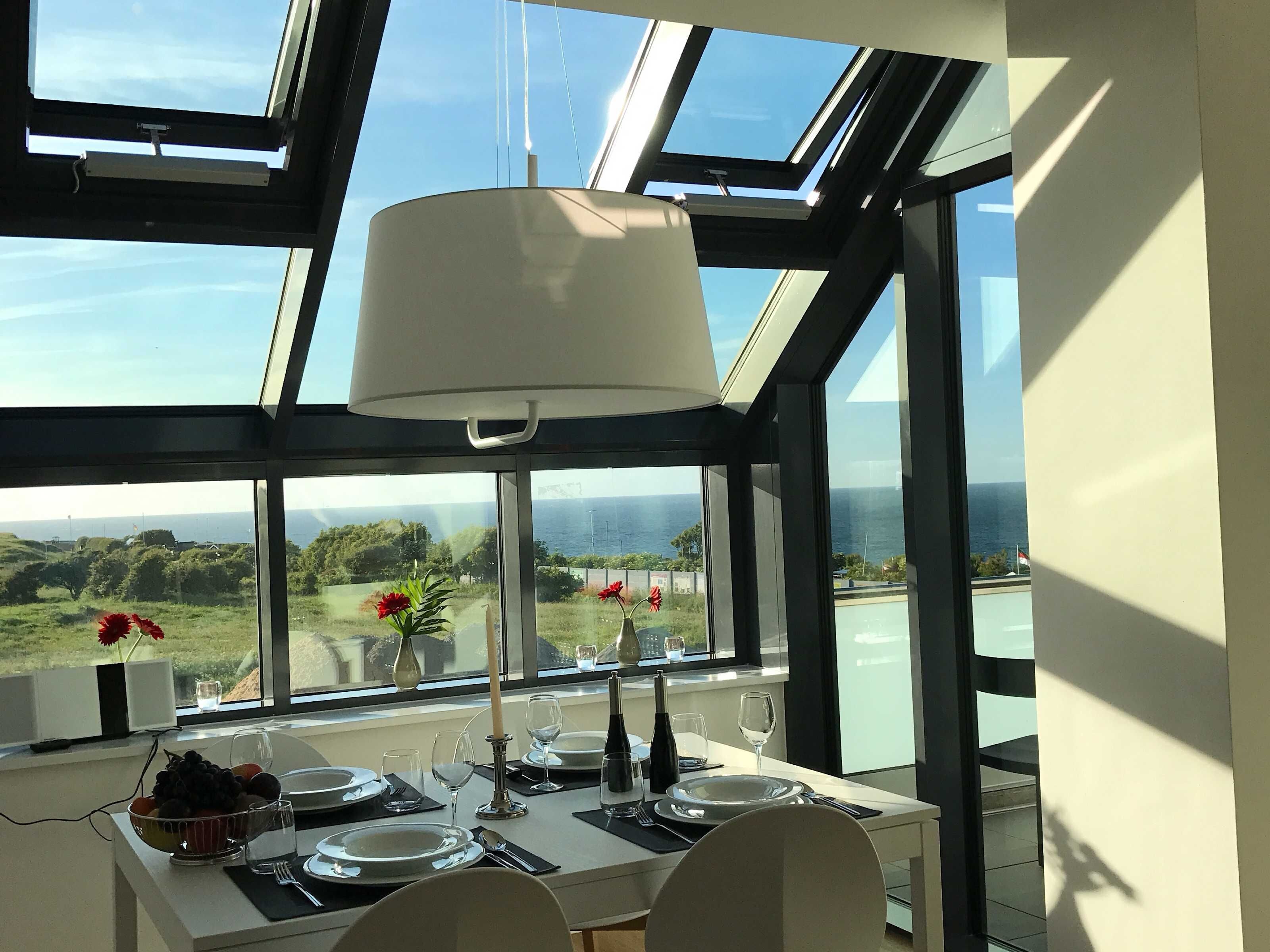 A dining area with a table set for two, large windows with a view of the sea, and a skylight above.