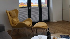A room with a yellow chair, a small table with a bottle and glass, and a view of buildings through a window. - Apartment 10 - gate to the sea (Helgoland)