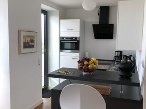 A modern kitchen with a black countertop, stainless steel appliances, and a bowl of fruit on the table. - Apartment 10 - gate to the sea (Helgoland)