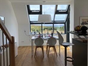 A dining area with a table set for two, a view of the countryside, and a skylight above. - Apartment 10 - gate to the sea (Helgoland)
