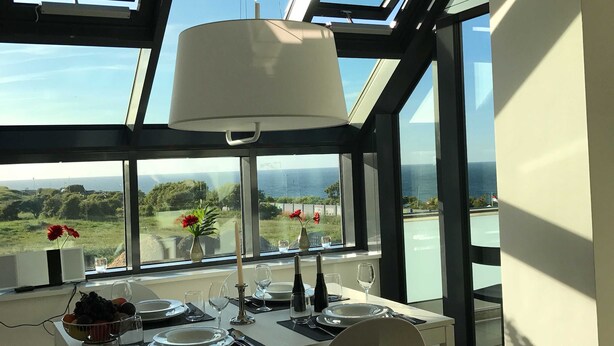 A dining area with a table set for two, large windows with a view of the sea, and a skylight above. - Apartment 10 - gate to the sea (Helgoland)