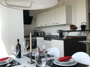A modern kitchen with white cabinets, a black countertop, and a dining area set with white plates, silverware, and wine glasses.