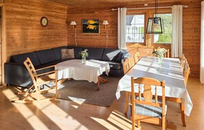 A cozy cabin interior with a wooden interior, a sofa, a dining table, and a view of the outside.